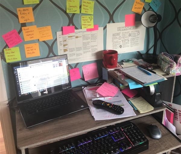 emmas desk with laptop and stick notes on wall behind